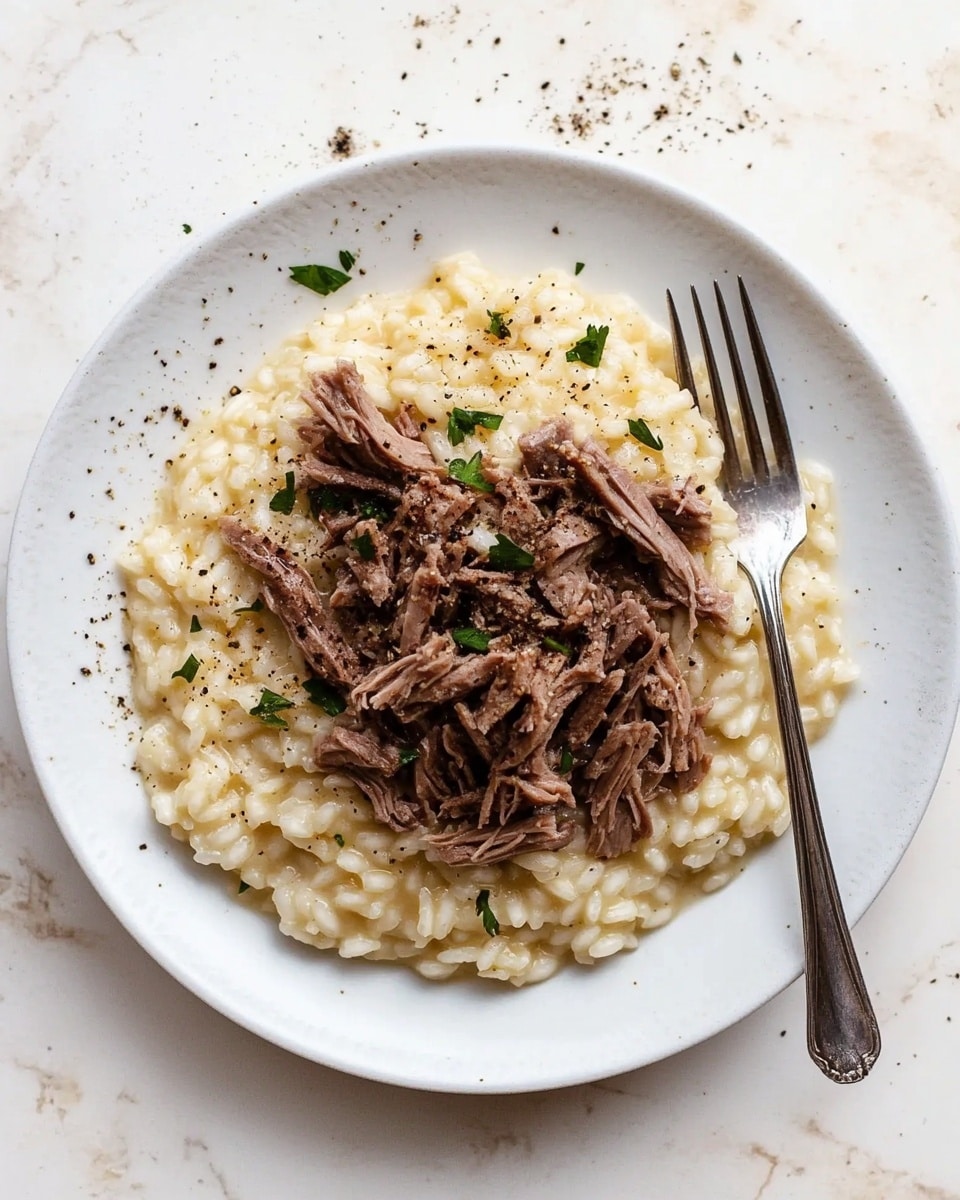 A round white plate sits on a white marbled surface with a creamy risotto base forming the bottom layer, showing soft, slightly shiny rice grains mixed with small bits of green herbs and a few black pepper specks. On top, there is a pile of dark brown shredded meat pieces, arranged loosely in the center of the risotto. A silver fork is placed on the right side of the plate, partially resting within the risotto and meat layers. The overall colors are warm creamy beige and rich brown, with a few scattered black pepper dots on the plate and surface. Photo taken with an iphone --ar 4:5 --v 6.1