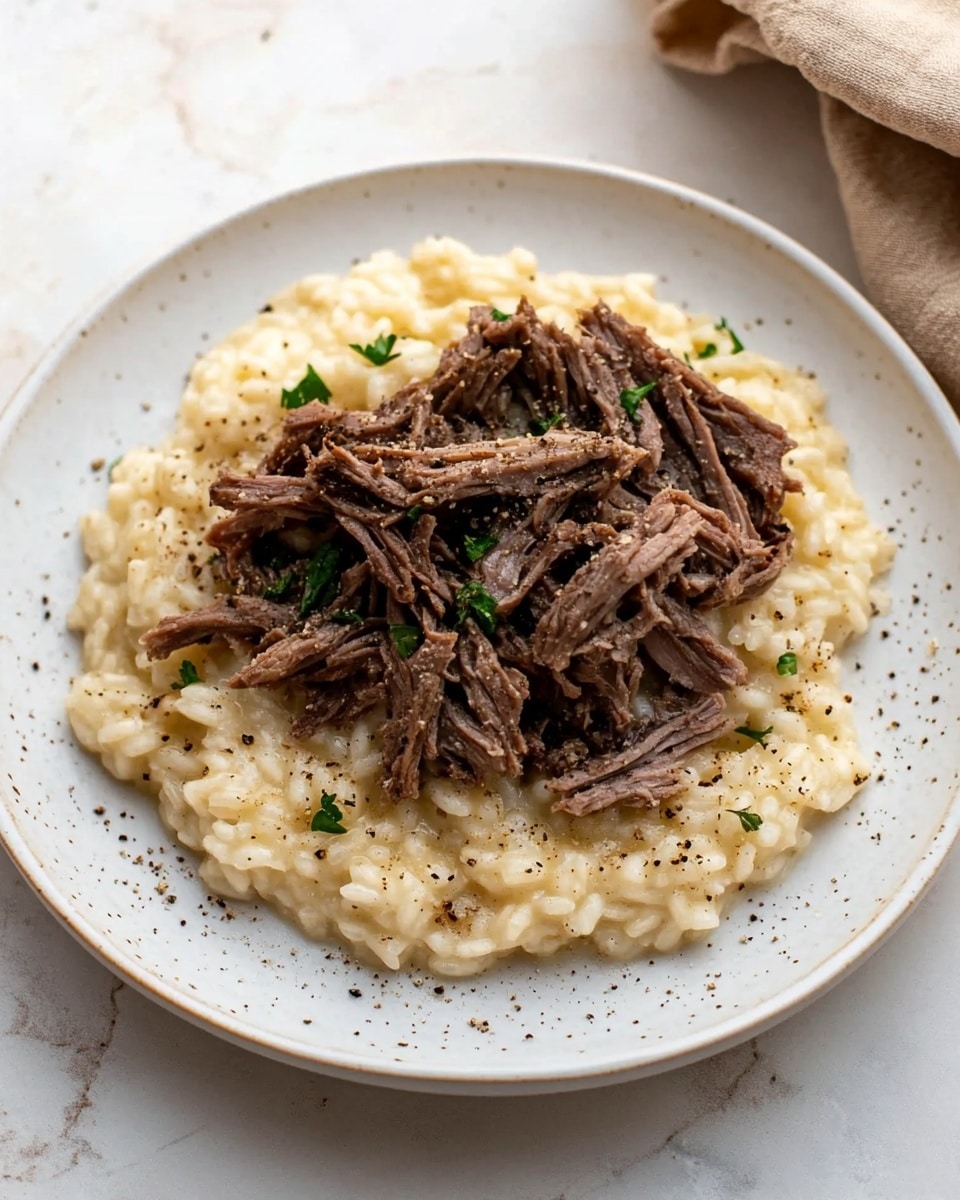 A white plate sits on a white marbled surface holding a dish with two main layers: the bottom layer is creamy risotto with a pale yellow color and small flecks of green herbs mixed in, creating a soft and slightly textured look; on top, there is a generous pile of shredded dark brown meat arranged loosely in the center, showing a fibrous and tender texture. The dish is lightly sprinkled with black pepper, adding small dots over the risotto and meat. A beige cloth with a brown stripe is placed folded in the upper right corner of the image. photo taken with an iphone --ar 4:5 --v 6.1