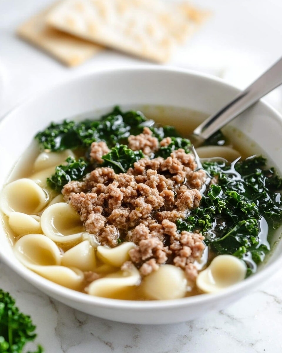 A white bowl sits on a white marbled surface filled with a clear broth soup. In the bowl, there is a layer of dark green leafy kale on one side. Next to the kale, there are light beige tortellini pasta pieces. On top of the pasta and kale is a layer of crumbled browned meat. The soup is sprinkled with white grated cheese and red chili flakes. A shiny silver spoon is placed on the surface next to the bowl. Photo taken with an iphone --ar 4:5 --v 6.1