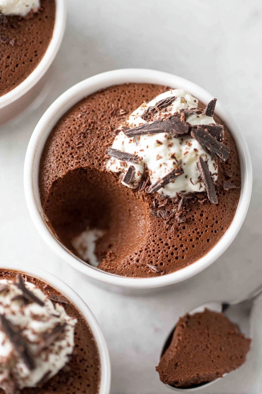 Decadent Chocolate Mousse, Chocolate Mousse Recipe, Easy Chocolate Dessert, Silky Chocolate Dessert, Rich Chocolate Treats - The image shows two white bowls filled with rich dark chocolate mousse, each topped with a small dollop of white cream and dark chocolate shavings scattered on top. One bowl in the center has a scoop taken out from it, revealing the airy, soft texture of the mousse inside. The mousse is thick and smooth with tiny bubbles visible, giving it a light look. The bowls are placed on a white marbled surface, adding a clean and simple background that highlights the dark brown color of the chocolate mousse. Photo taken with an iphone --ar 2:3 --v 7