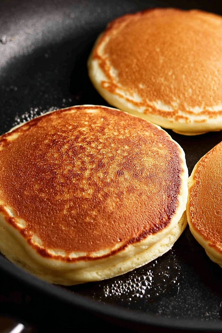 Fluffy Ricotta Pancakes with Strawberries and Maple Syrup, ricotta pancake recipe, easy breakfast recipes, fluffy pancake ideas, strawberry breakfast recipes - A stack of four thick, golden-brown pancakes sits in the center of a white plate on a white marbled surface. The pancakes are fluffy with a slightly crispy edge, and syrup is being poured from above, flowing down the sides in a shiny amber stream. The top pancake is adorned with a dollop of cream and several bright red sliced strawberries, with more strawberry pieces scattered around the plate. In the foreground, a woman's hand holds a fork that has just taken a bite from a pancake, showing the soft, airy inside texture. Photo taken with an iphone --ar 2:3 --v 7