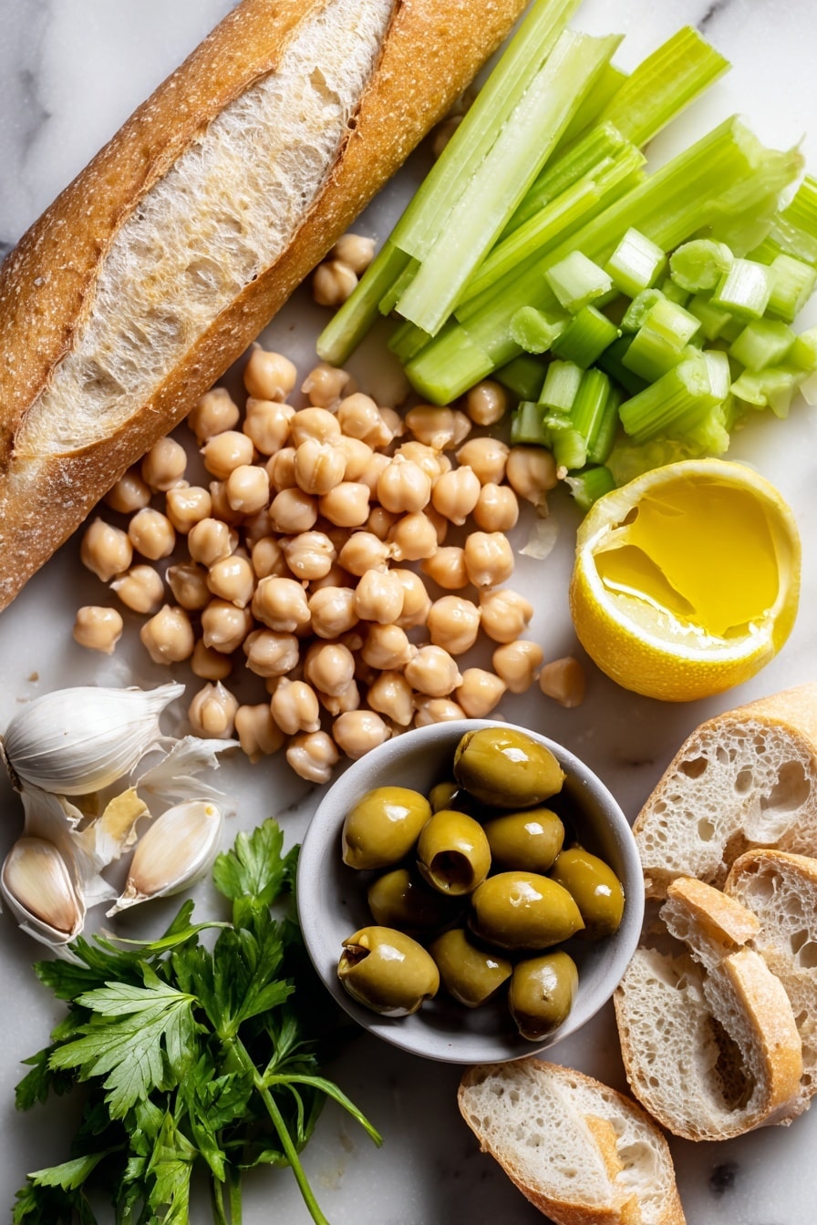 Greek Crostini, Greek Crostini Recipe, Mediterranean Appetizer, Easy Greek Bites, Healthy Crostini Ideas - Flat lay of plump, light beige chickpeas with a smooth, round texture, a small pile of bright green celery pieces finely diced showing crisp edges, shiny dark green kalamata olives sliced to reveal their glossy interior, a fresh medium garlic clove with creamy white skin and slight papery texture, a halved lemon bright yellow with visible juicy segments, glistening golden extra virgin olive oil in a small natural puddle catching light, and several baguette slices showing a crusty golden-brown exterior with a soft, airy white crumb inside, all naturally arranged with some celery sprigs loosely scattered to add freshness, placed on white marbled surface, photo taken with an iphone --ar 2:3 --v 7