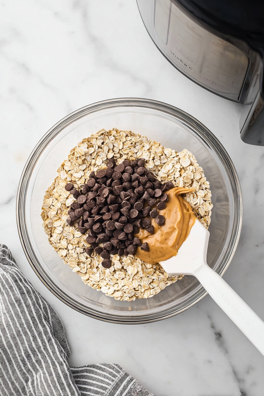 Giant Air Fryer Oatmeal Cookie, air fryer oatmeal cookie, quick oatmeal cookie, easy air fryer desserts, homemade oatmeal cookie - Two round golden-brown cookies with visible cracks lay on white parchment paper over a wooden board, each sprinkled with shiny dark chocolate chips that create dark spots on the surface. The cookie at the bottom is being held gently by a woman's hand from the right side. Around the board, there are scattered oats and chocolate chips on a white marbled surface, with a measuring cup filled with dark chocolate chips placed in the upper right corner and a bowl full of oats in the lower left corner. A striped cloth is partly visible on the right side. photo taken with an iphone --ar 2:3 --v 7